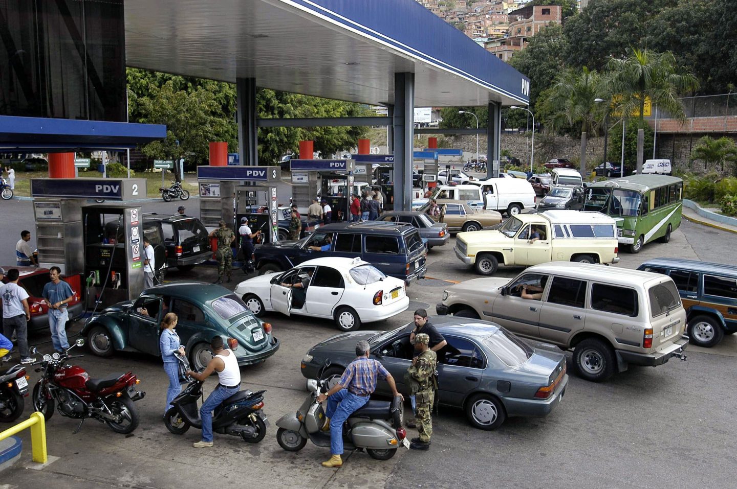Cars and motorcycles wait in long lines at a gas station.