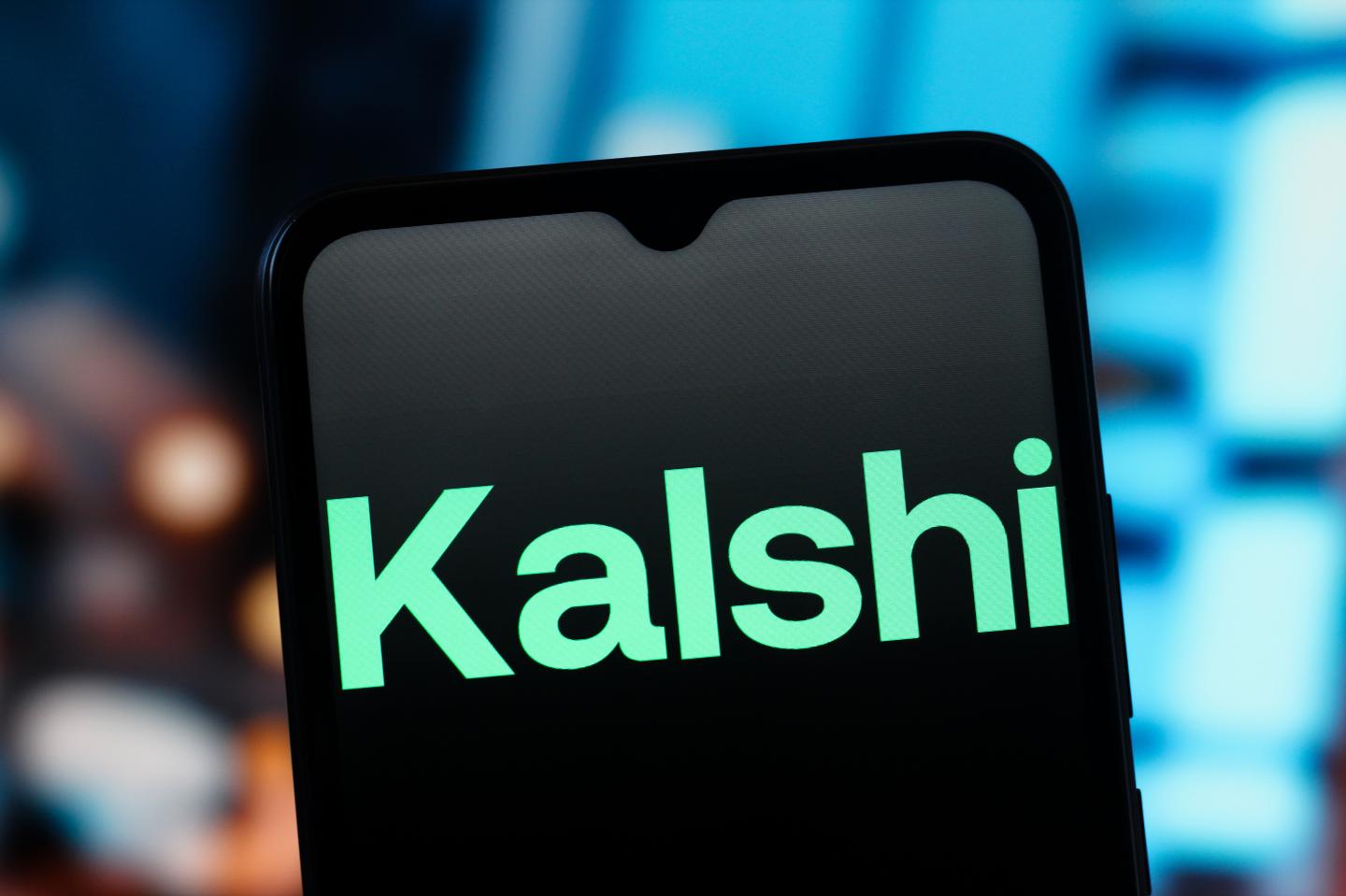 A phone displays the company logo for Kalshi.
