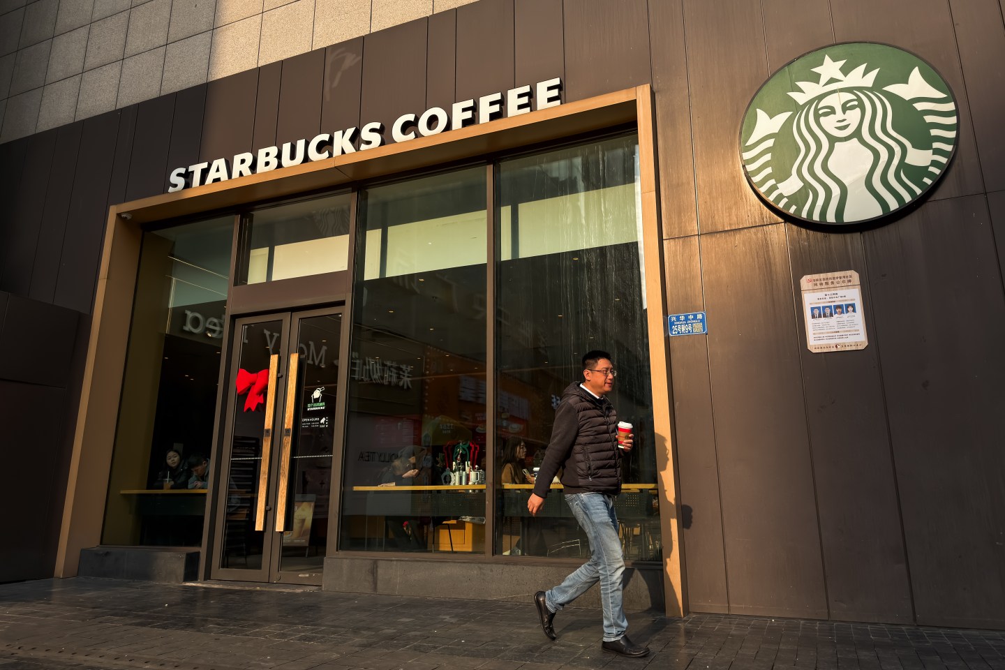 CHONGQING, CHINA NOVEMBER 26: A man walks past a Starbucks coffee store with a drink in hand on November 26, 2025, in Chongqing, China. Starbucks continues to operate thousands of outlets across China, serving one of its largest international markets. (Photo by Cheng Xin/Getty Images)