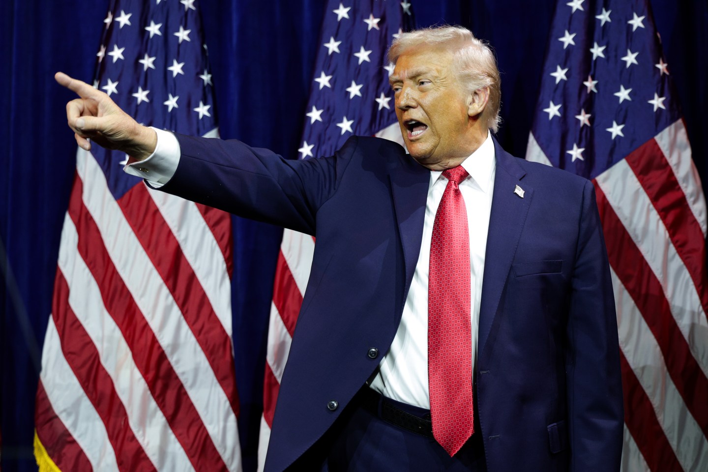 President Donald Trump pointing in front of American flags.