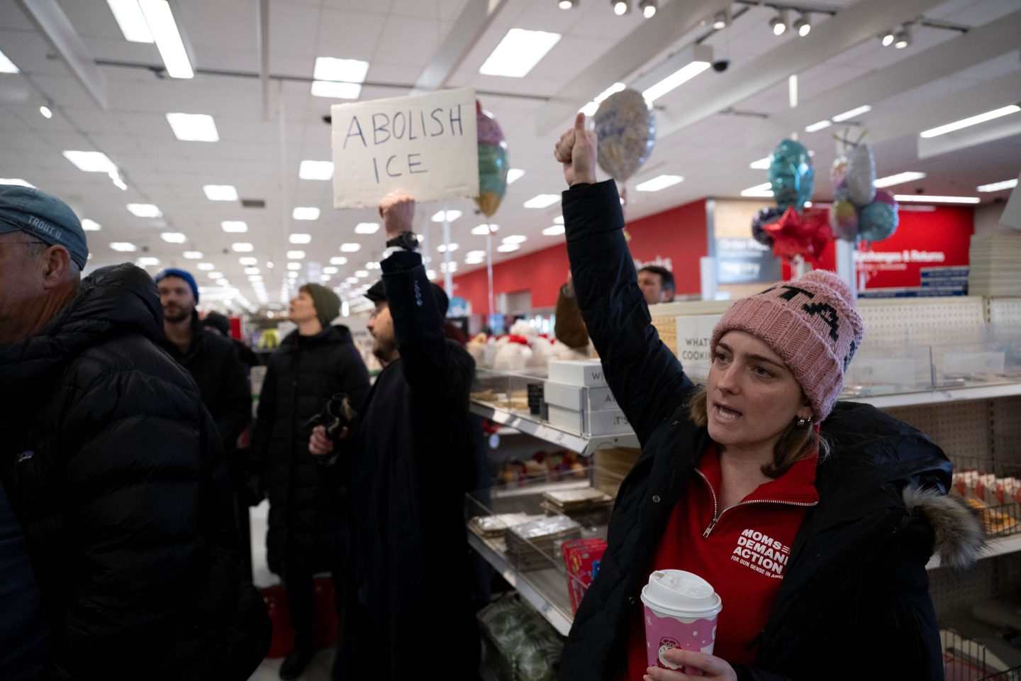 A woman stands in a target with her fist in the air. A man behind her holds an "Abolish ICE" sign.