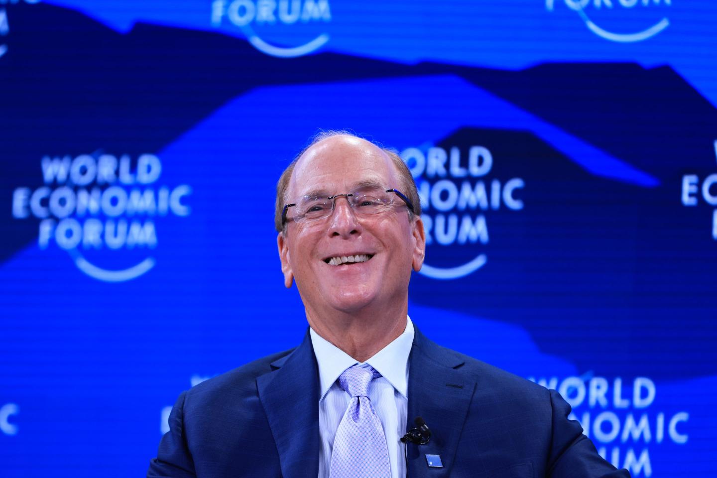 Man with glasses smiling before a blue background.