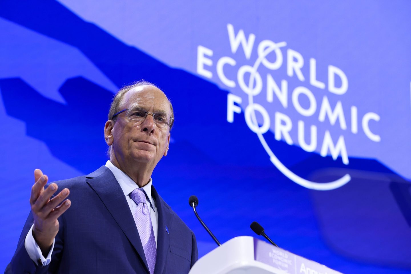 Larry Fink speaks behind a podium and in front of a blue "World Economic Forum" background.