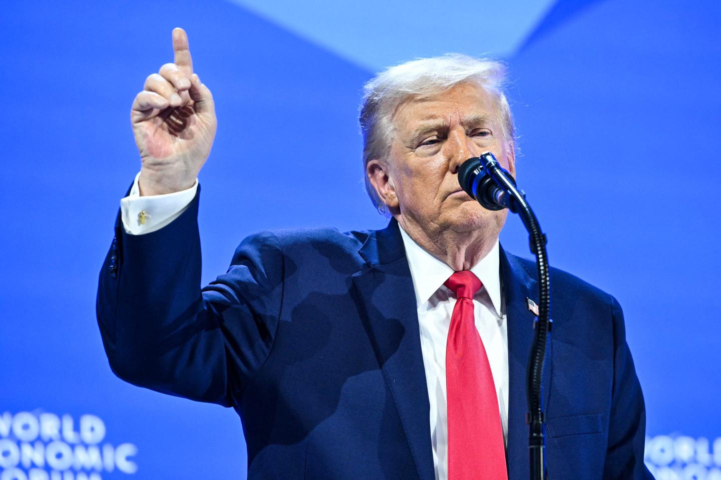 Trump, standing behind a microphone, puts his pointer finger in the air.