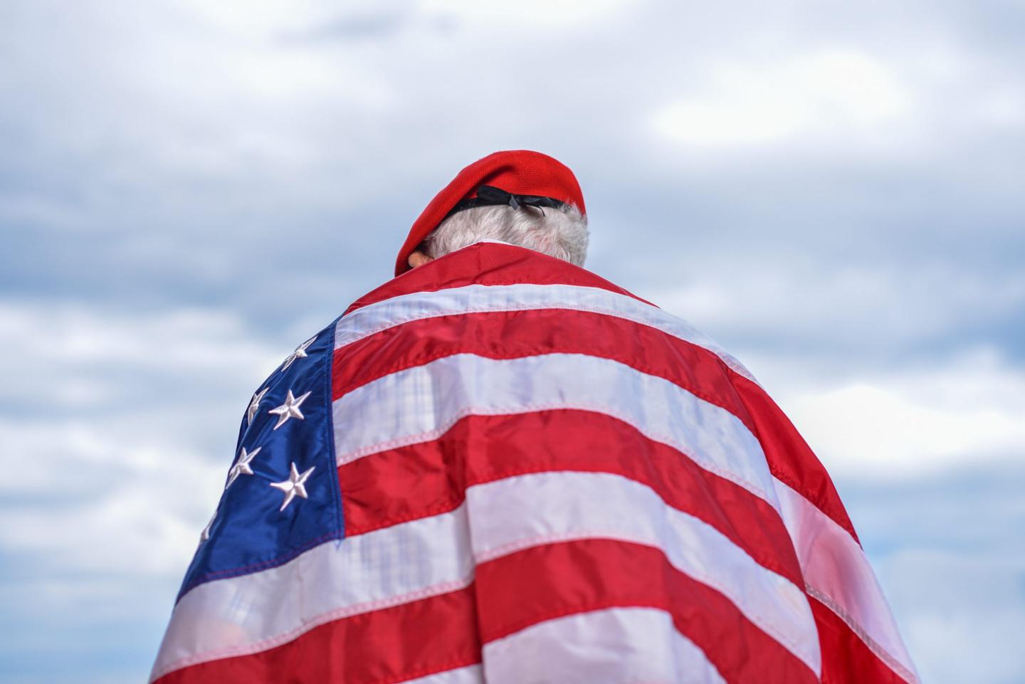 An older man wears an American flag around his shoulders
