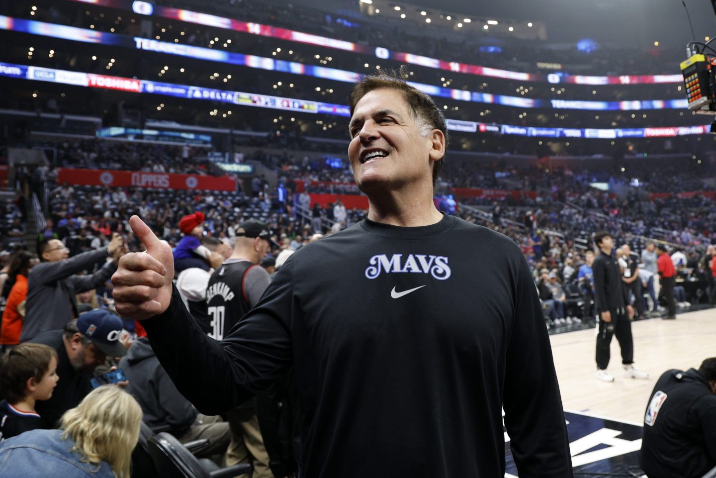 Mark Cuban, standing in a basketball arena, gives a thumbs up.