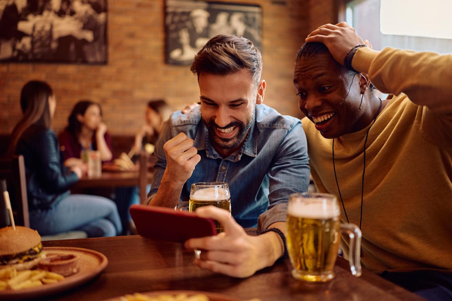 Two men in a sports bar are happy as they look at a phone