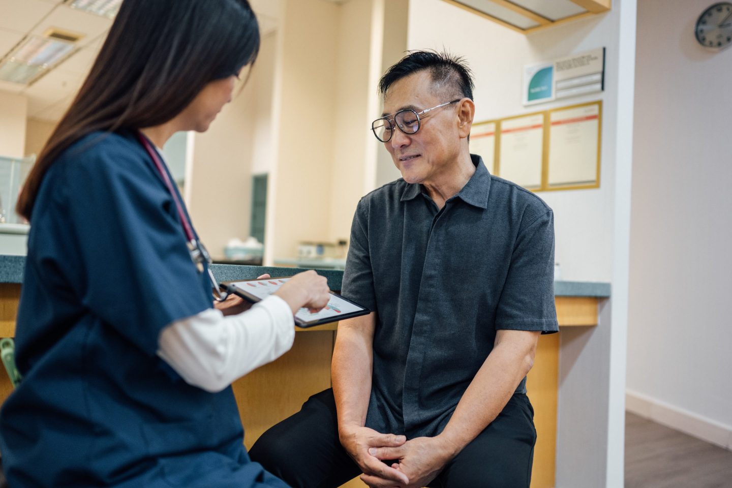 A shot of an Asian female doctor discussing a patient's healthcare data report on a digital tablet with an Asian male patient in a hospital.