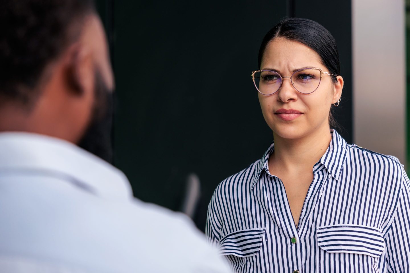Two colleagues engage in a serious discussion, with the woman’s furrowed brow and displeased expression reflecting frustration and dissatisfaction. The moment captures workplace tension and the emotional challenges of professional interactions.