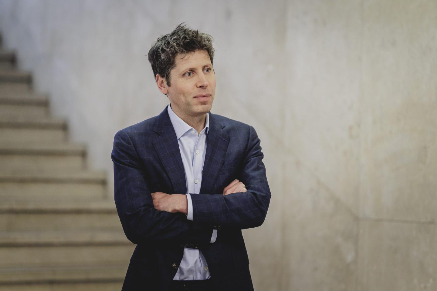 Sam Altman is standing with his arms folded.