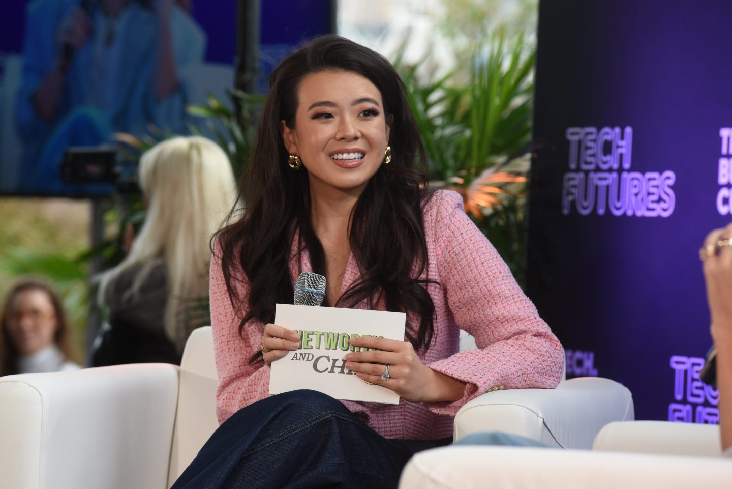 Tu speaks onstage holding a microphone and notecards