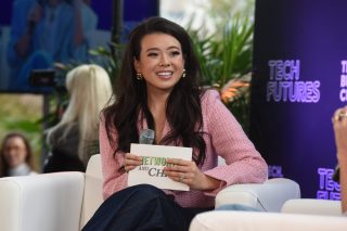 Tu speaks onstage holding a microphone and notecards