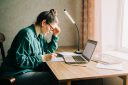 Stressed out woman looks at her notebook and computer while sitting at a desk.