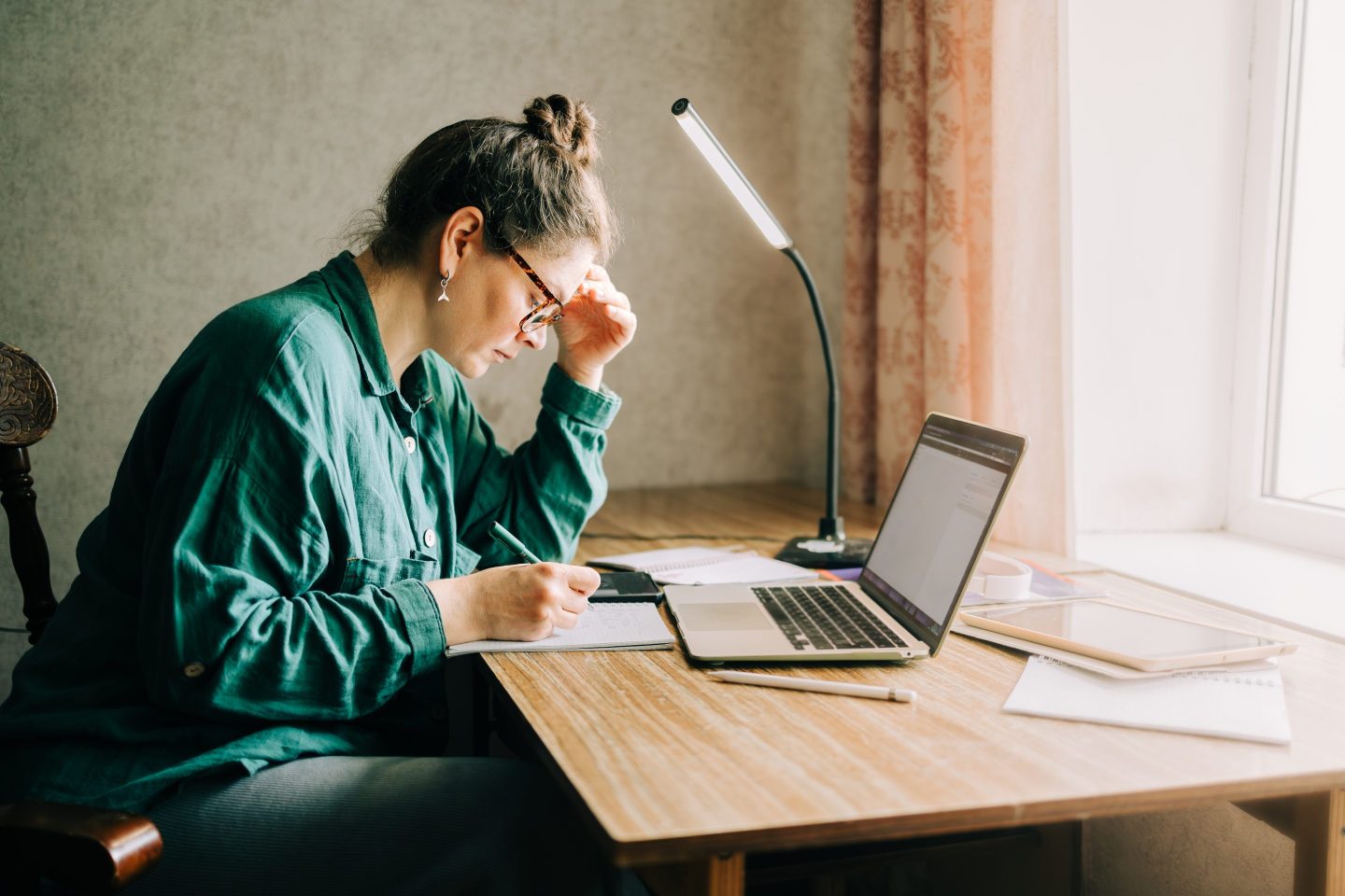 Stressed out woman looks at her notebook and computer while sitting at a desk.