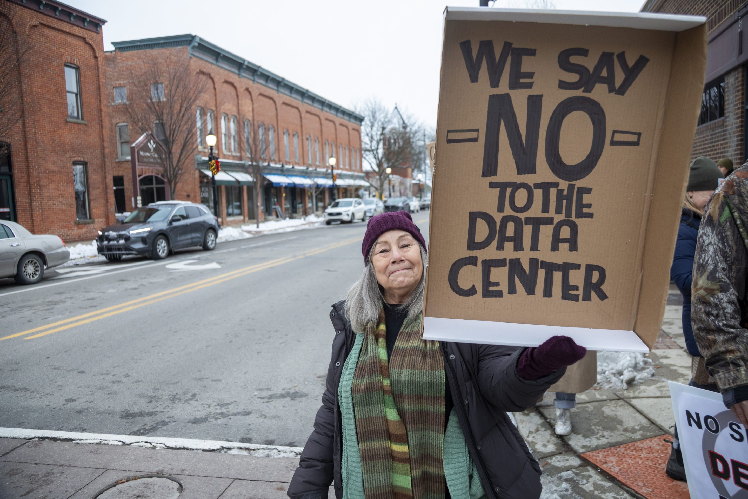 A woman on the street holding a carboard sign reading, "We say NO to the data center"