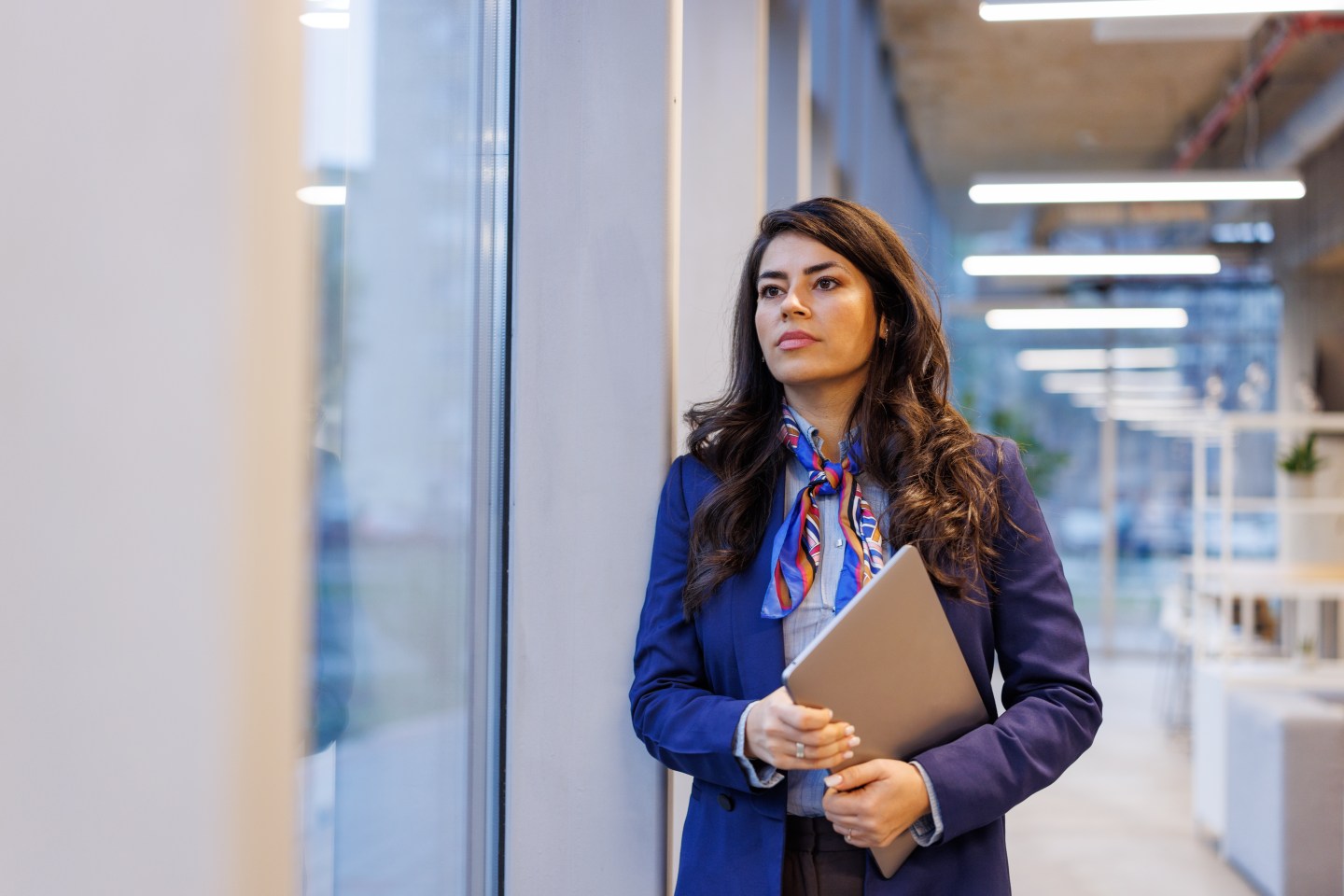 Businesswoman holding a laptop, looking away, reflecting on future success