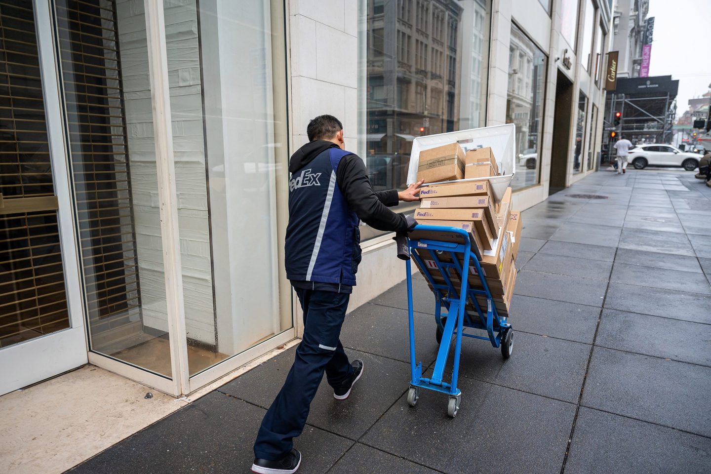 A FedEx employee pushes a dolly with several boxes on it down a street