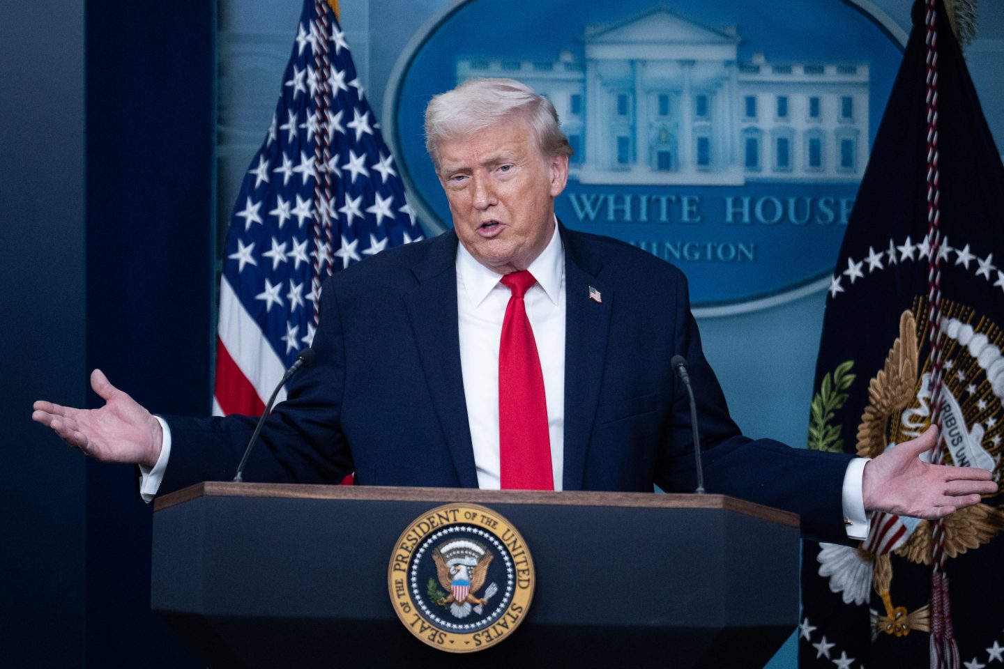 Donald Trump shrugs as he stands behind the podium in the White House briefing room.