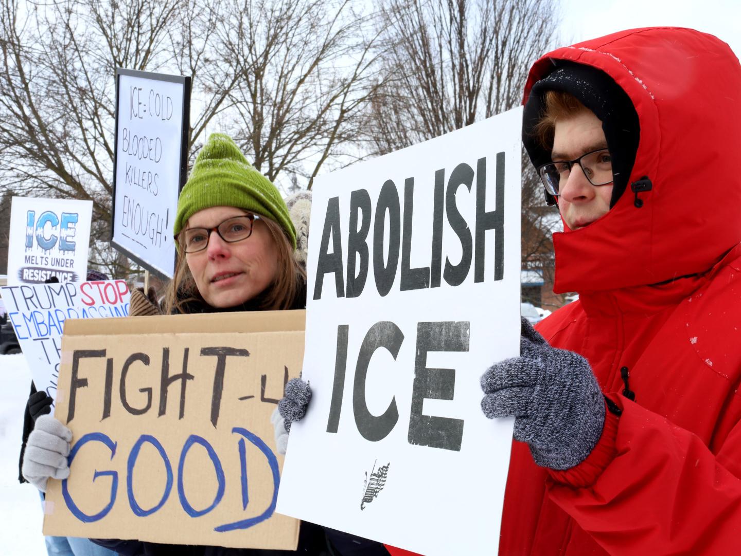 Protesters in coats and hats hold up signs protesting ICE