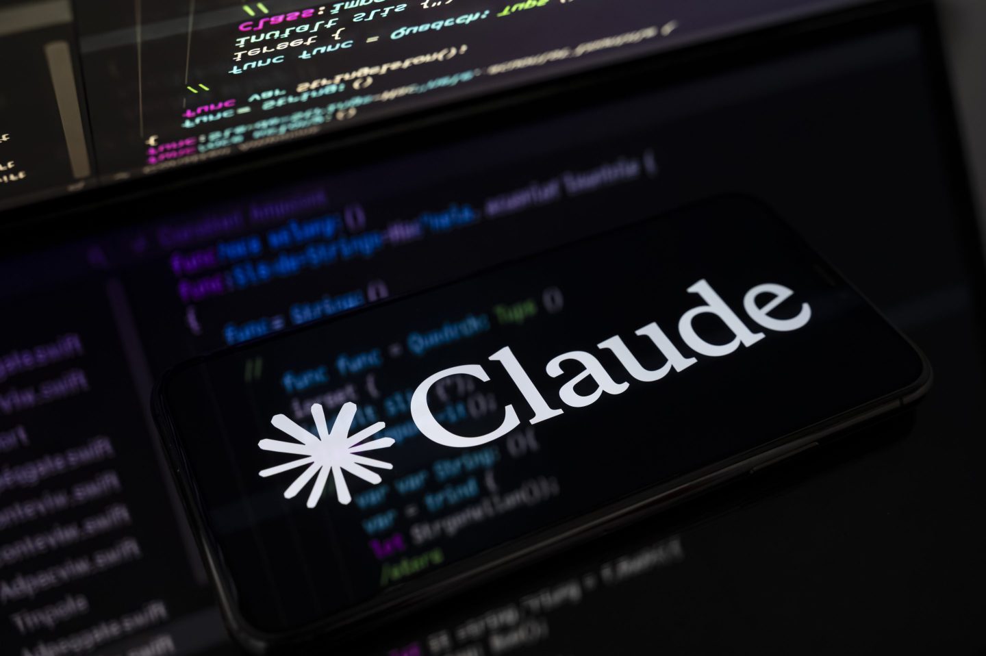 The Claude AI logo is displayed on the screen of a smartphone placed on a reflective surface onto which lines of computer code are projected. Following the release of Claude Opus 4.6 on February 5, Anthropic continues to challenge its main competitors in the generative AI market in Creteil, France, on February 6, 2026. (Photo by Samuel Boivin/NurPhoto via Getty Images)