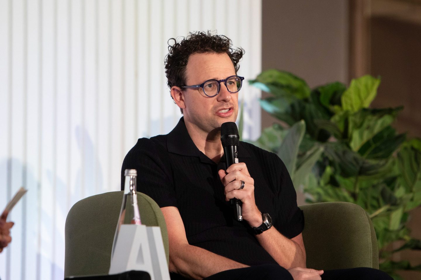Dario Amodei holds a microphone and speaks while seated.