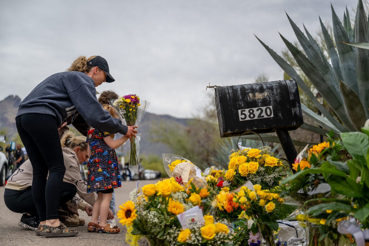 a woman and girl put flowers down in front of Nancy Guthrie's home