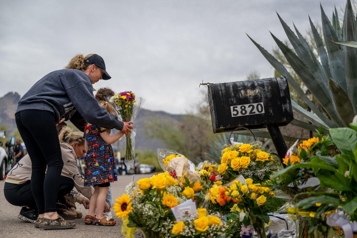 A woman and girl put flowers down in front of Nancy Guthrie’s home