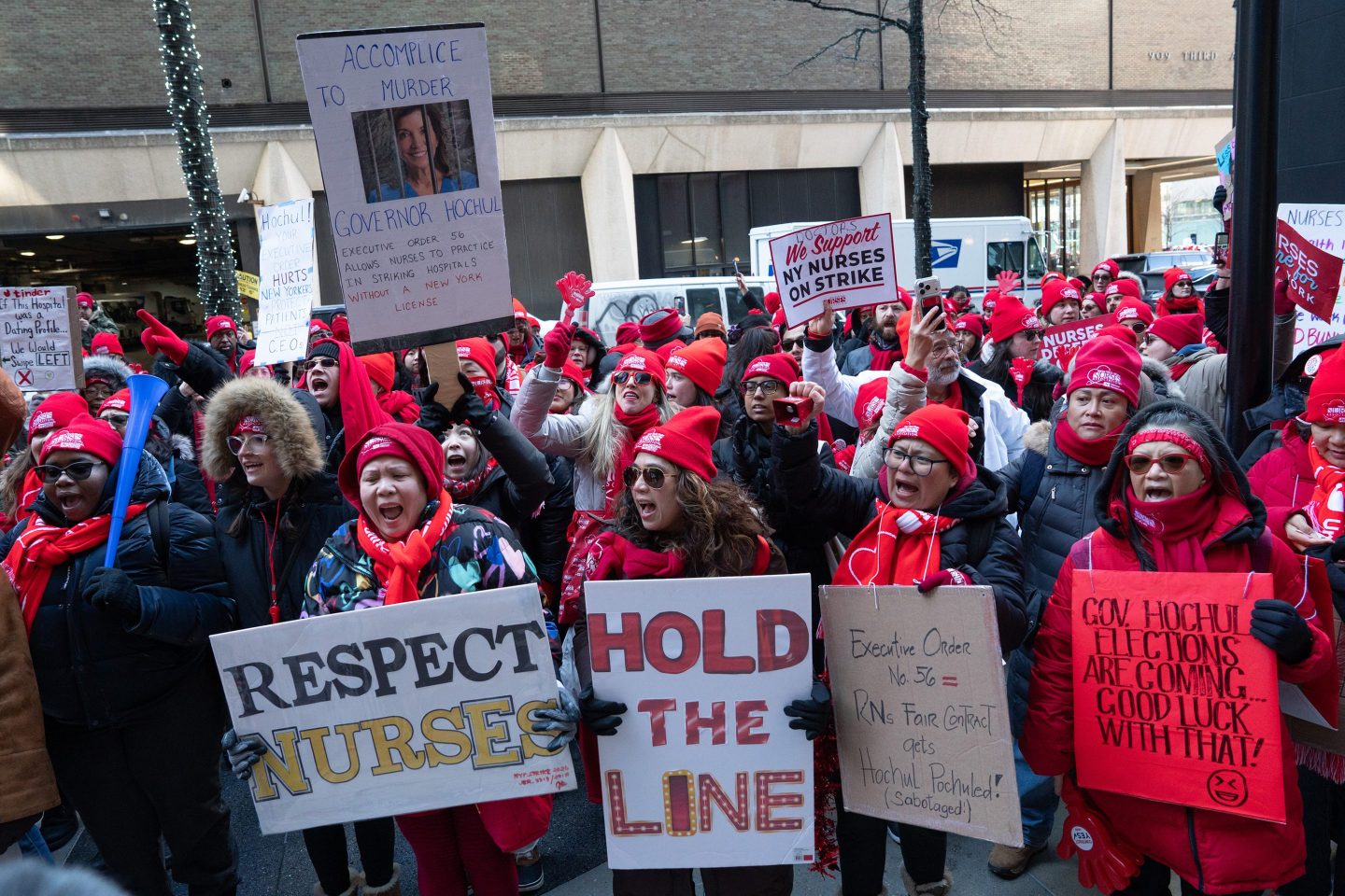 People, mostly women, stand outside chanting with signs supporting nurses.