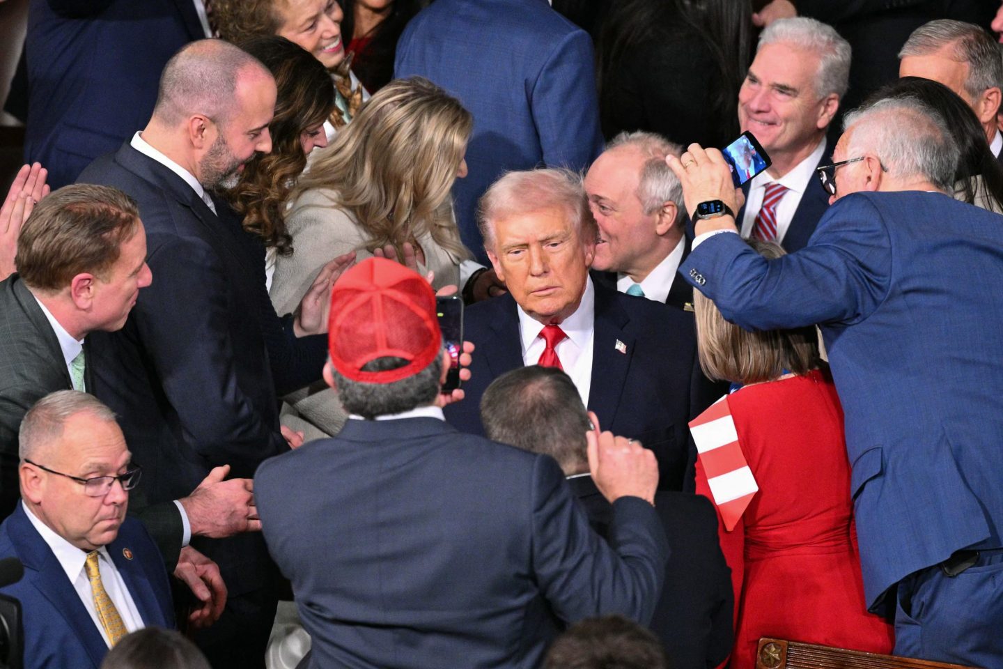 Donald Trumpm in a suit and red tie in a swarm of people.