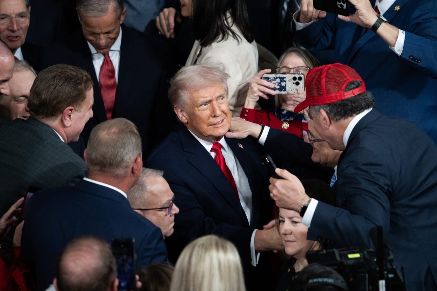 A man wearing a red hat shakes Trump's hand in a crows