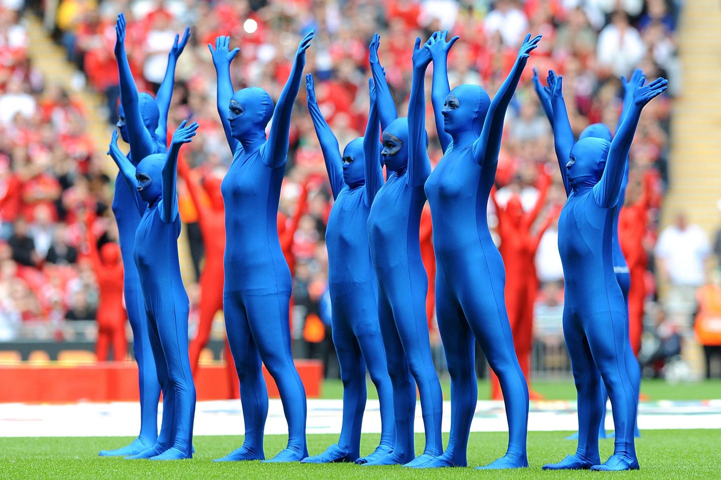Performers in Morph suits on a football field pre-match