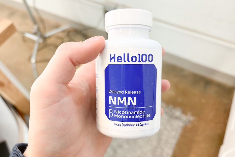A close-up of a hand holding a bottle of Hello100 Delayed Release NMN.