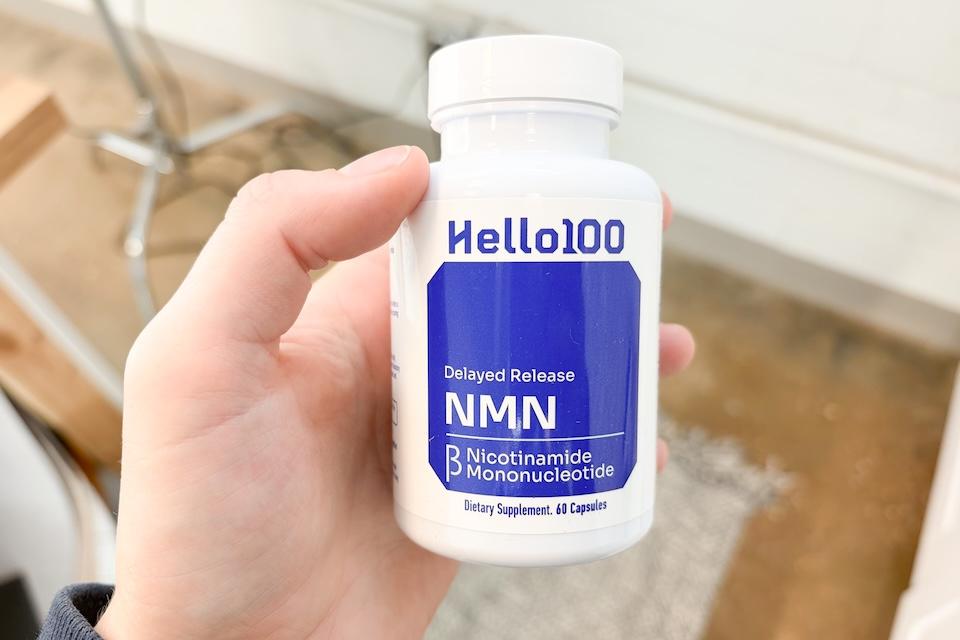 A close-up of a hand holding a bottle of Hello100 Delayed Release NMN.