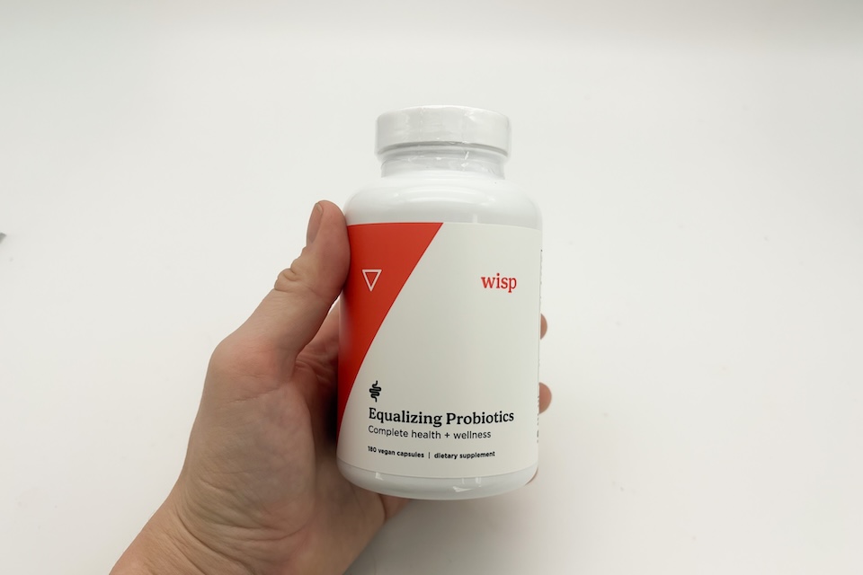 A close-up shot of a hand holding a bottle of Wisp Probiotics.