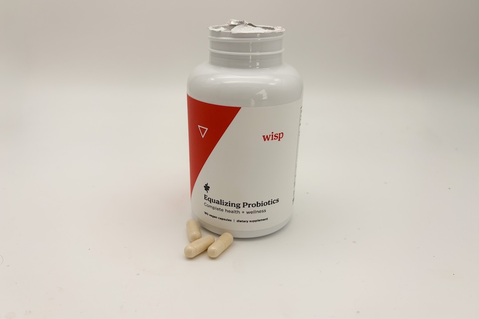 An open bottle of Wisp Probiotics. Three capsules are resting next to it.