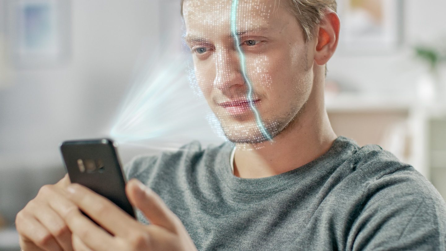 Photo of a young man holding a smartphone having his face scanned