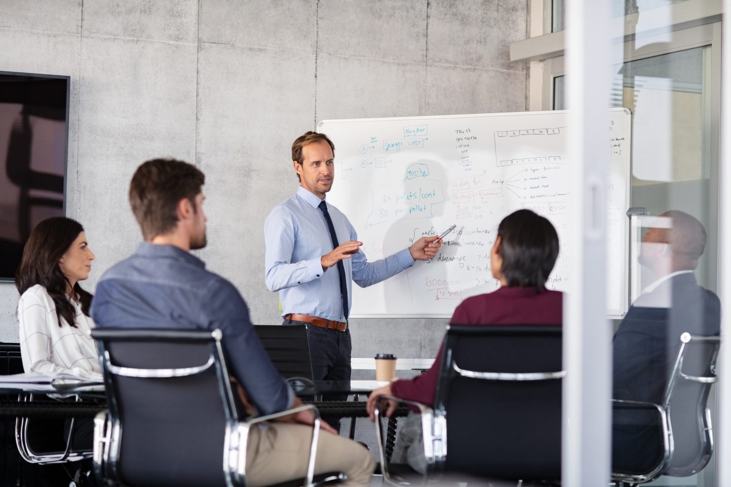 A man points to a white board during a meeting