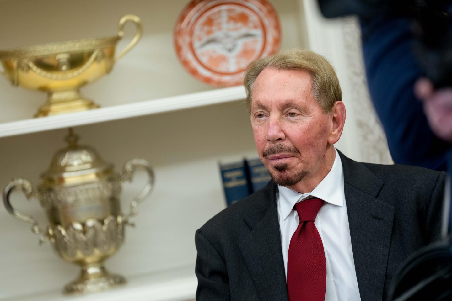 Man with facial hair looking to the side wearing a suit and tie.