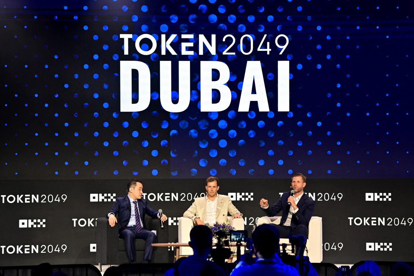 three men speak on conference stage