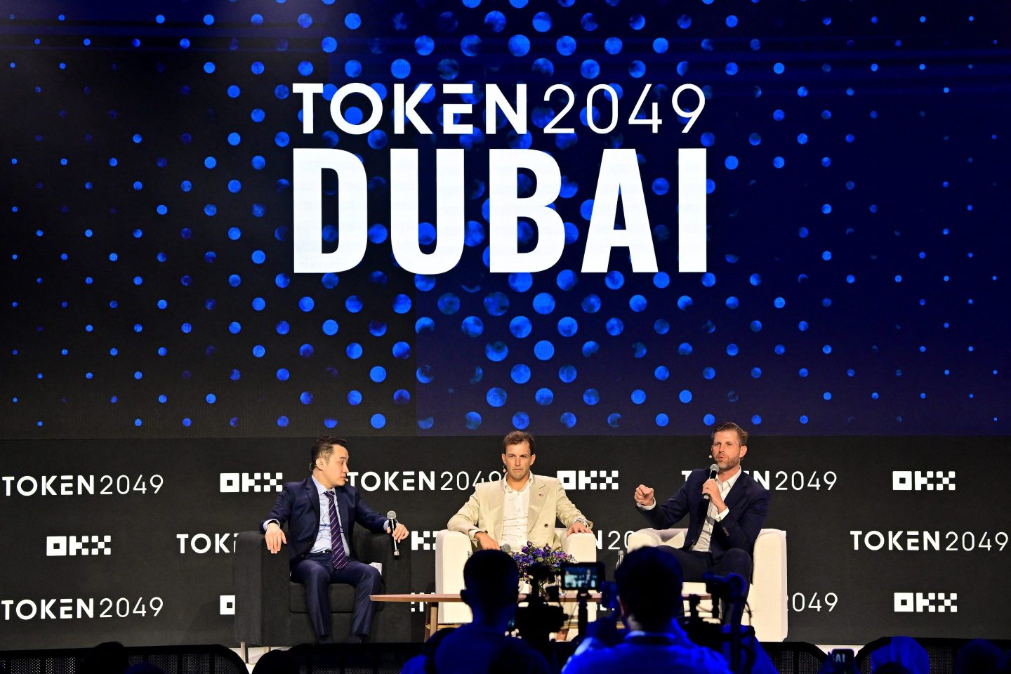 three men speak on conference stage