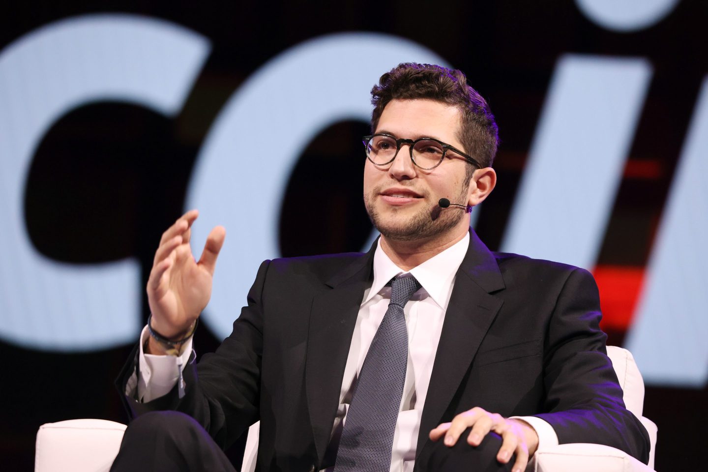 Brandon Lutnick, chairman of Cantor Fitzgerald, sits in a white chair wearing a suit and speaking.