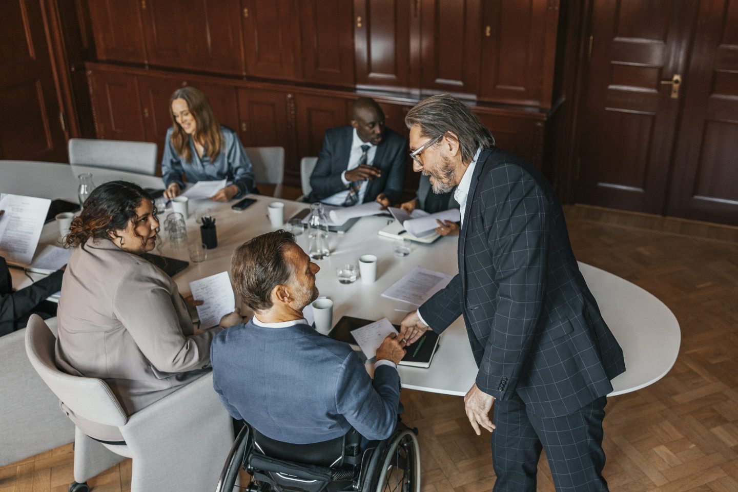 High angle view of businessman assisting colleague sitting in wheelchair at an office.
