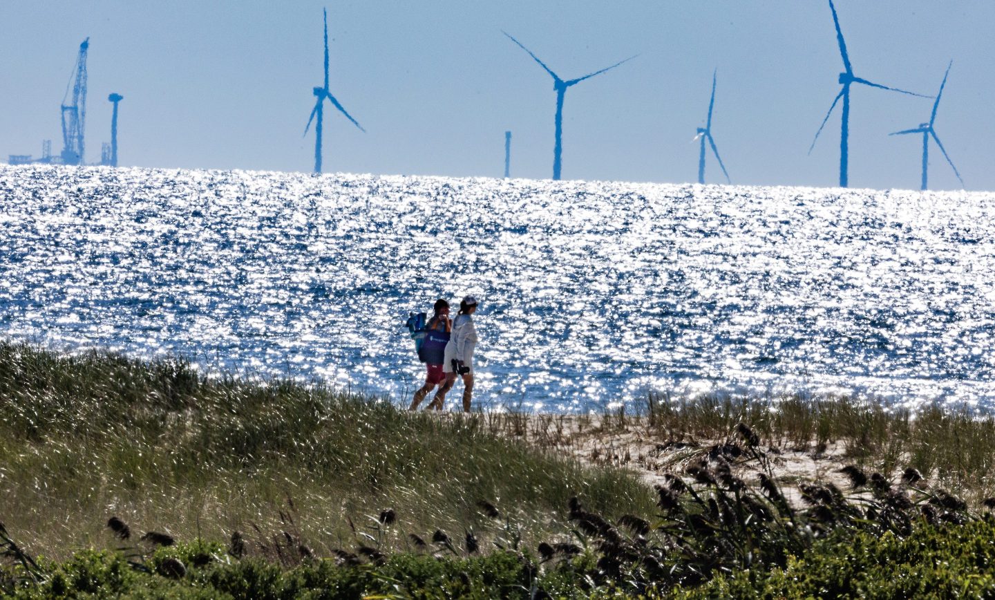 People walk in front of a wind farm.