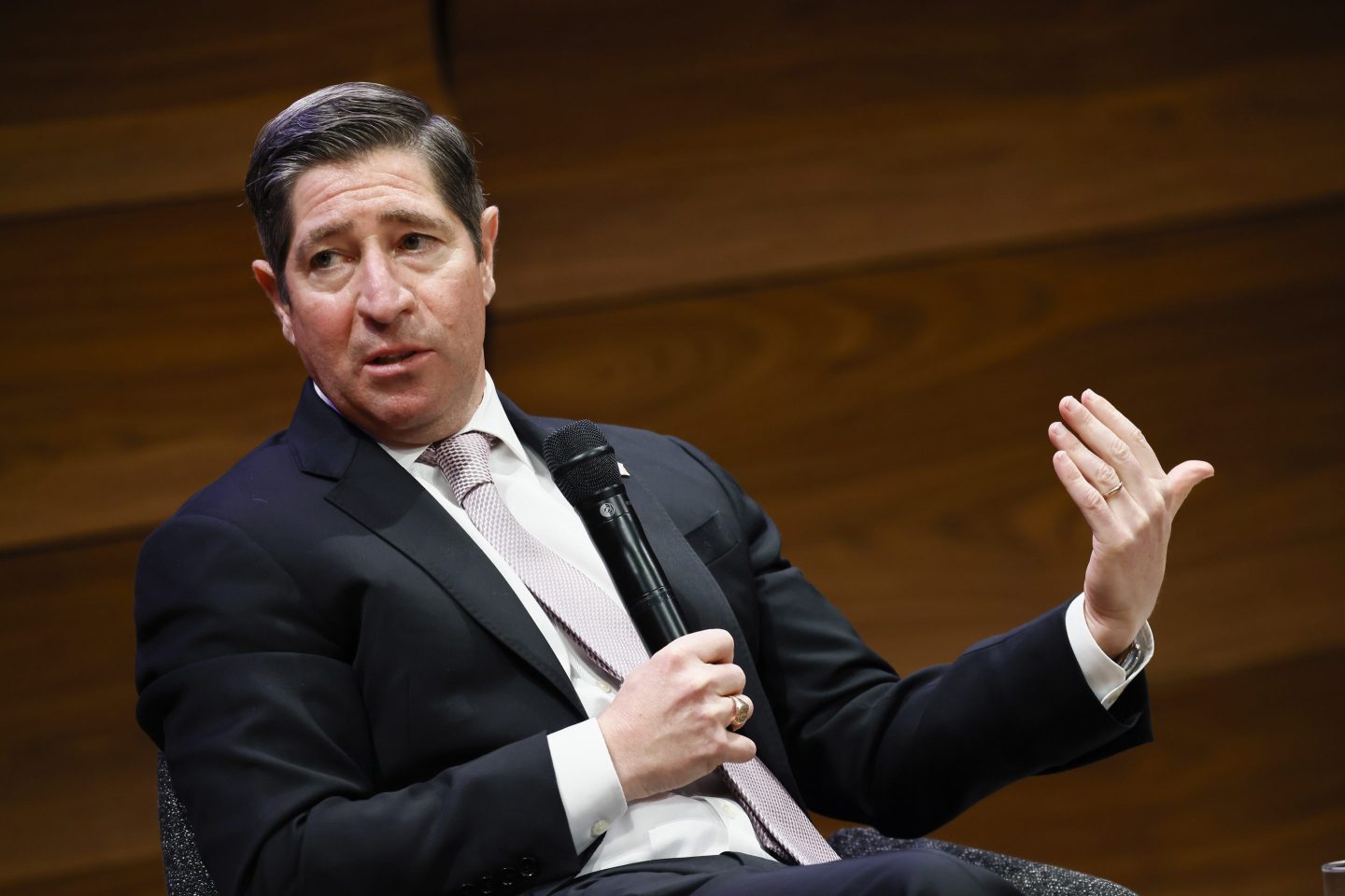 Scott Kupor sits and holds a microphone in phone hand and gestures with the other.