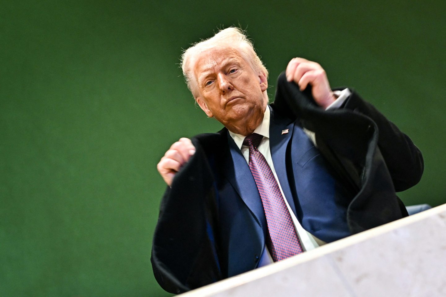 Trump flipping his jacket up against a green backgroun
