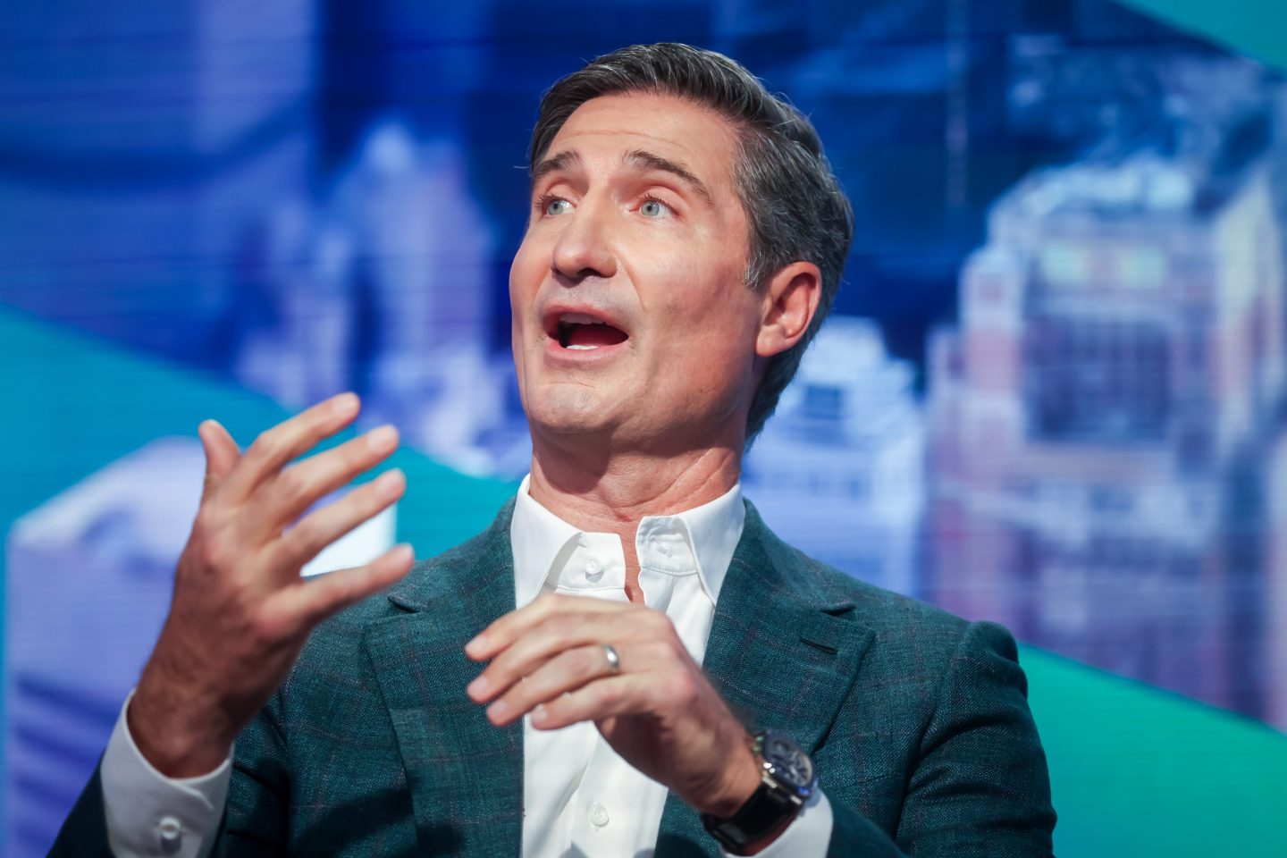 Brian Niccol speaks and gestures in front of a blue and green background.