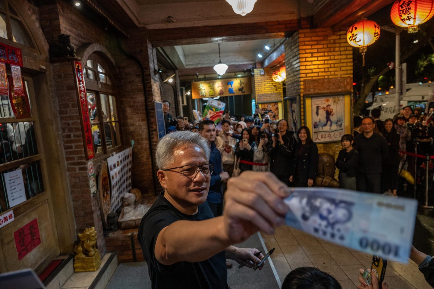 Huang passes a $1,000 New Taiwan dollar bill to a child in the crowd.