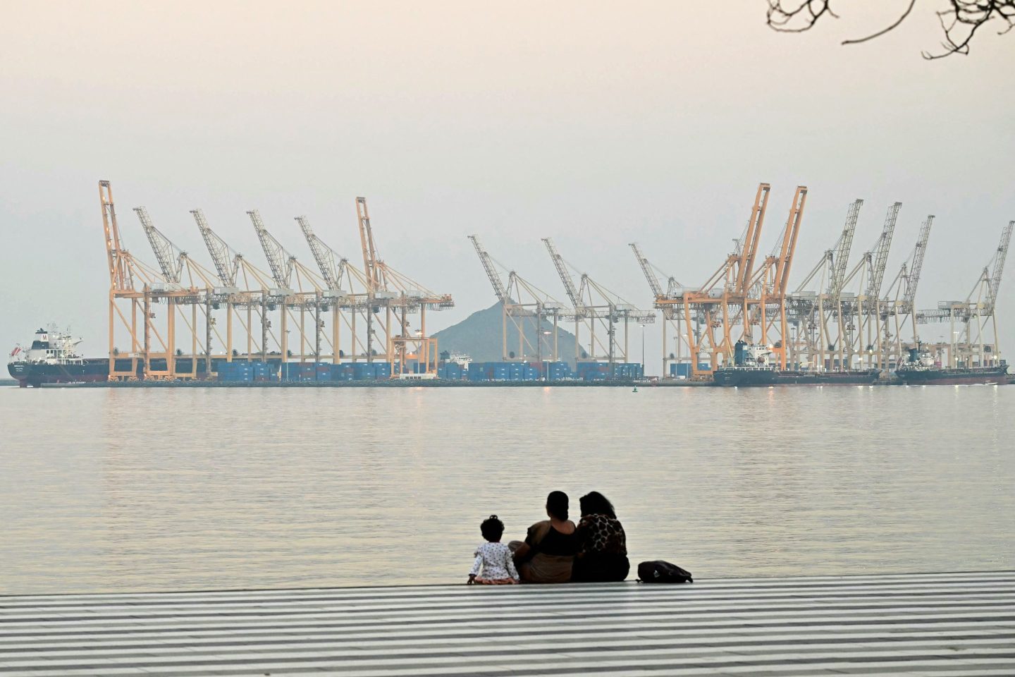 A family sits against the backdrop of a dockyard off coast city of Fujairah, in the Strait of Hormuz in the northern Emirate on February 25, 2026. (Photo by Giuseppe CACACE / AFP via Getty Images)