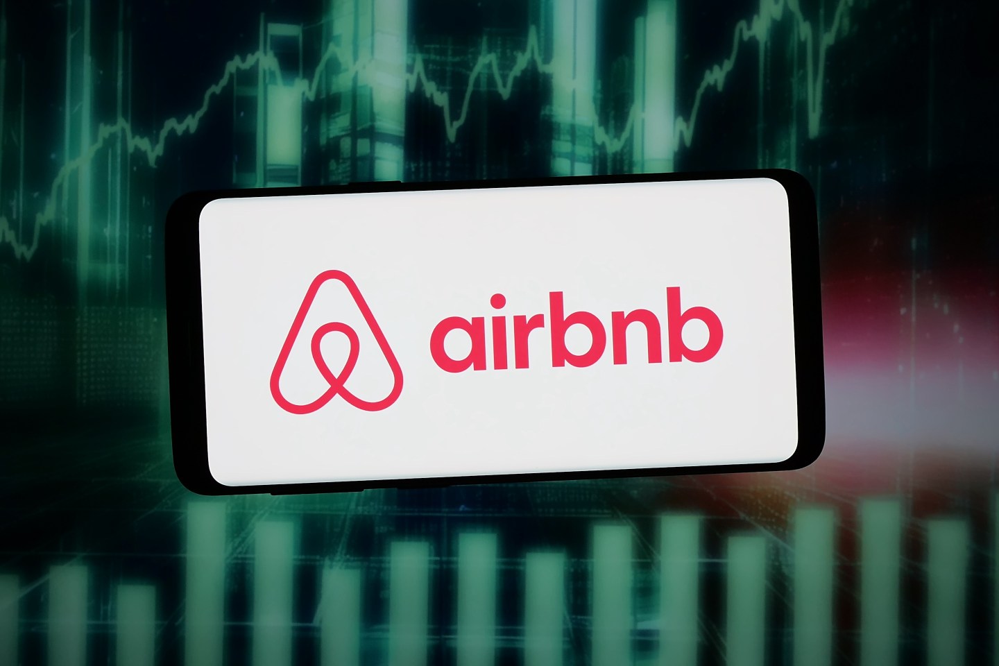 In this photo illustration, the logo of US homestay marketplace company Airbnb Inc. is displayed on a smartphone in front of abstract background on computer screen.
