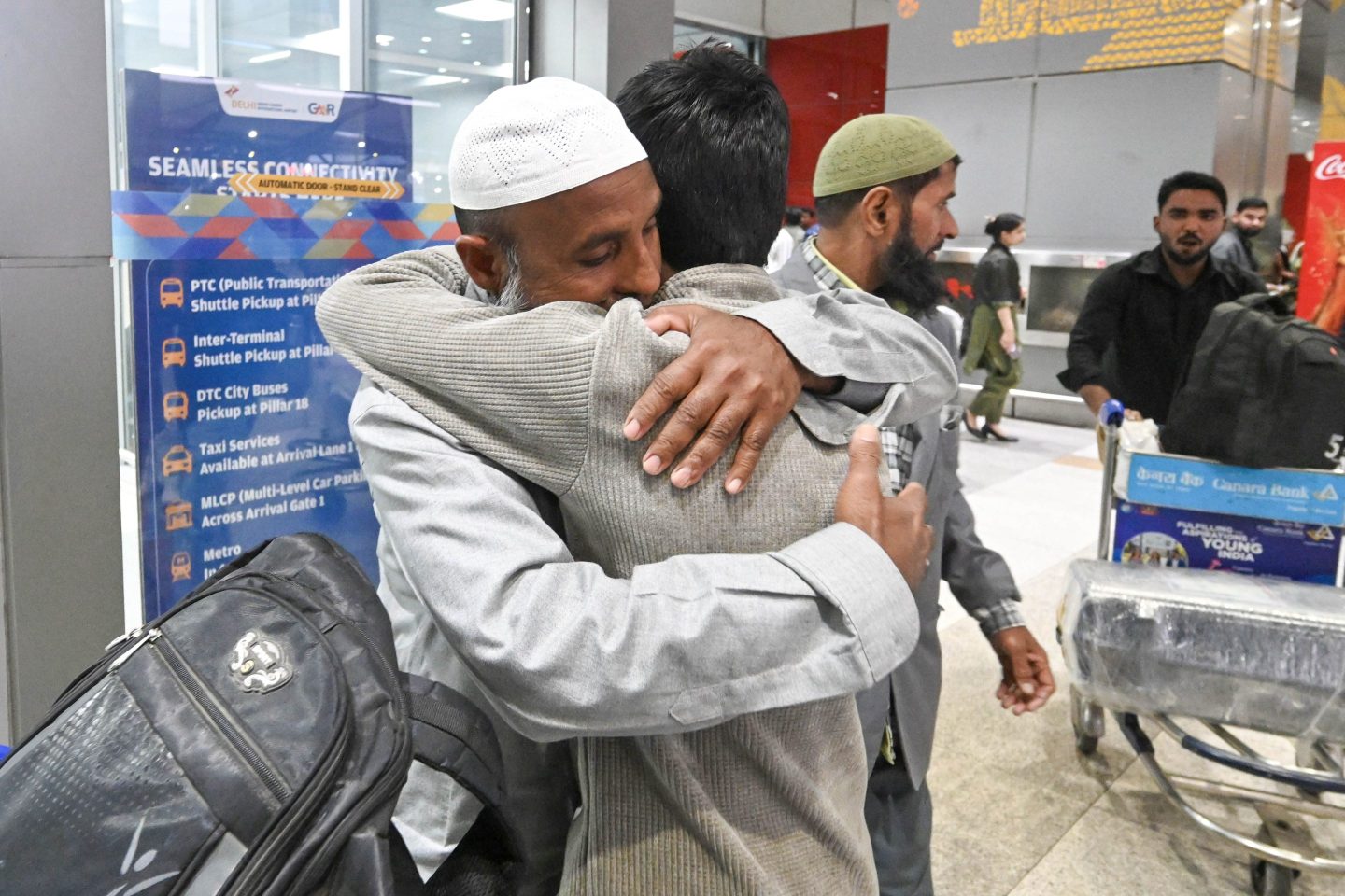 An older and younger man embrace at an airport.